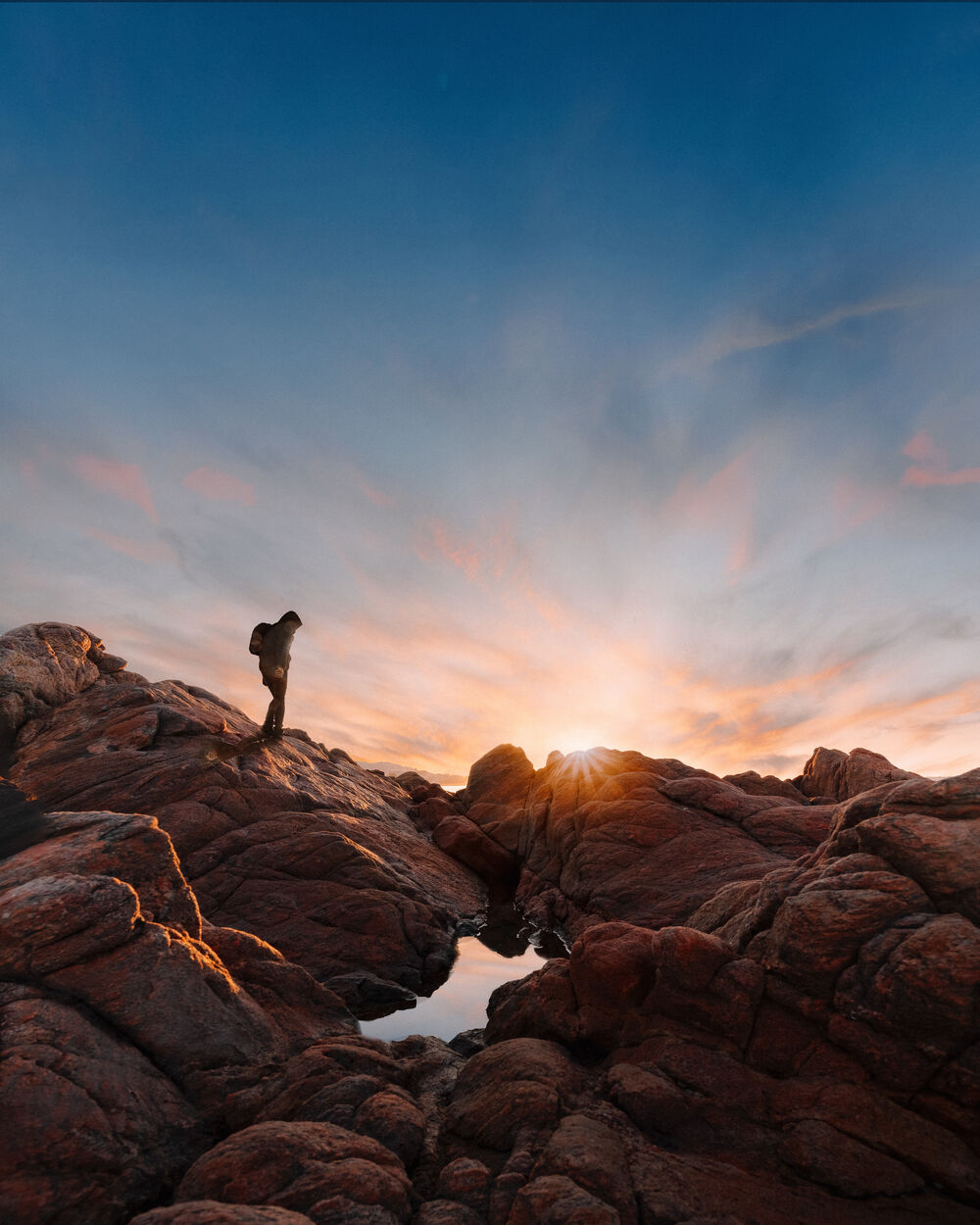 A hiker standing on rocks at sunrise